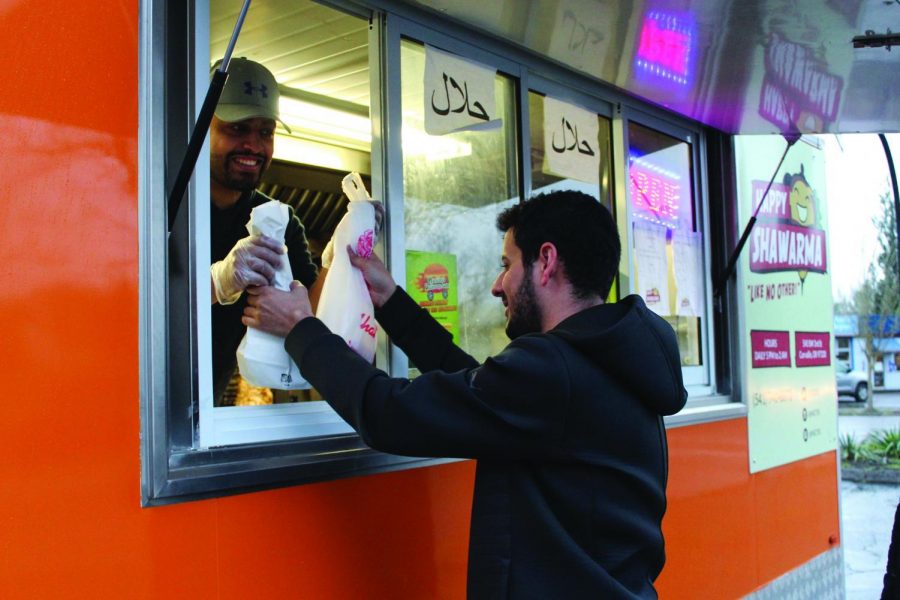 Ali Aldubaini handing food to Sultan Alanazi from the Happy Shawarma window. Aldubaini opened Happy Shawarma in February 2017 after he noticed a need in the community for the Middle Eastern dish.