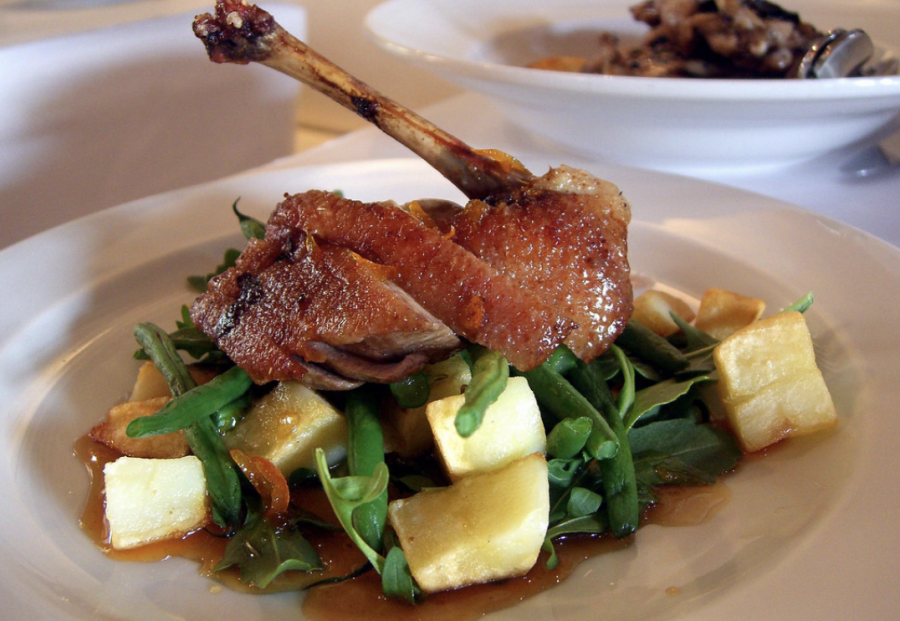 Cooked duck is garnished with orange sauce and accompanied with a side.