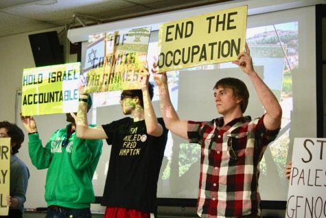 Student protesters hold up their signs in front of the former IDF soldier’s presentation. Blocking the view of the audience.
