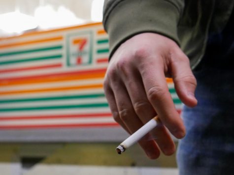 A hand holding a lit cigarette in front of 7 Eleven. One of the new laws in Oregon has increased the tax on cigarettes and cigars as well as established a tax on e-cigarettes and vaping products.