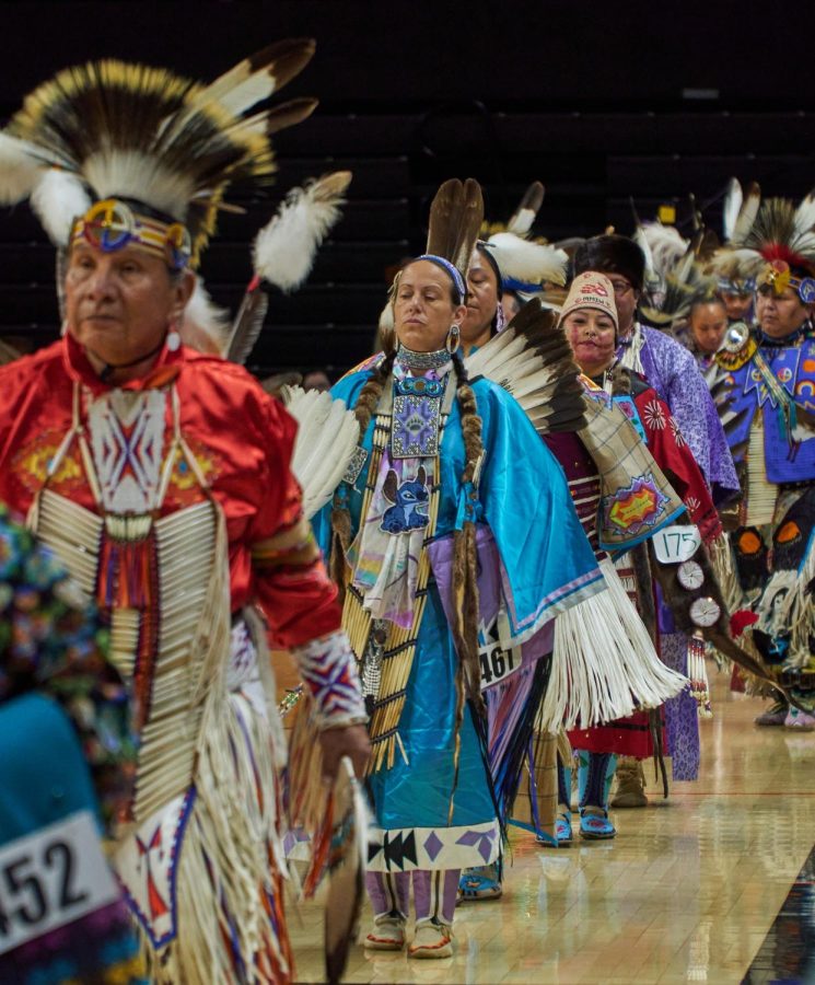 A group of men and women dance into the arena during Grand Entry at the OSU 2023 Spring Pow-wow at Gill Coliseum on May 20. Both the men and women pictured are Traditional Style dancers, signified by the nuances in their regalia. 