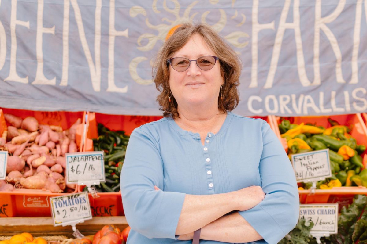 A photo illustration shows Rebecca Landis (she/her) posing in front of the Beene Farm stand of the Corvallis Farmers Market on September 30, 2023. Landis has managed the nonprofit association of  Corvallis-Albany Farmers Markets, presiding as the market director.
