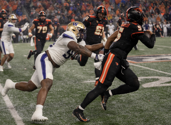 Oregon State quarterback DJ Uiagalelei (#5) rushes downfield shielding off an University of Washington defender in a  22-20 Beaver loss at home on Nov. 18, 2023.