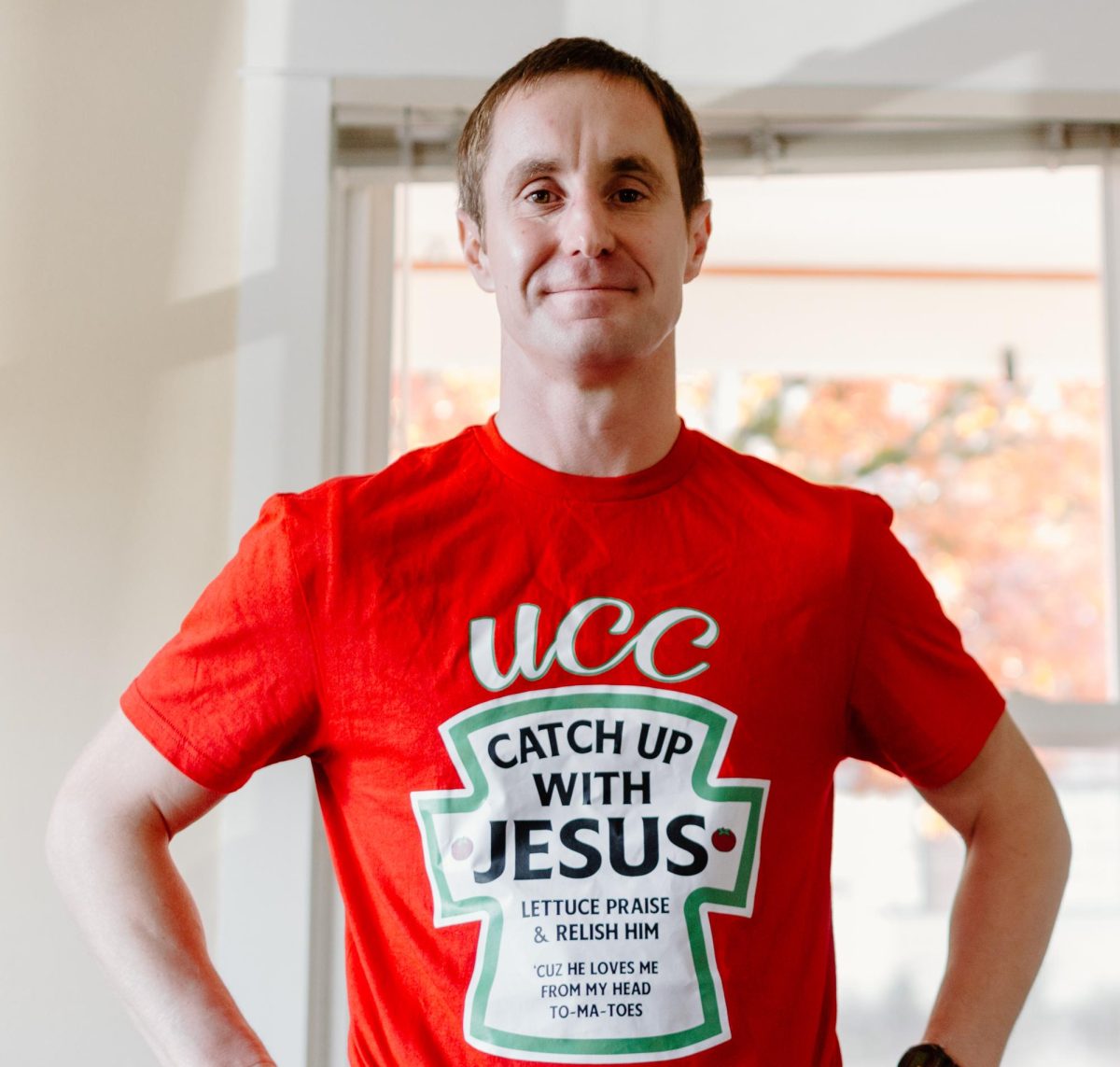 Campus minister Josh Stutzman poses in the University Christian Center wearing their shirt design of the year on November 7, 2023