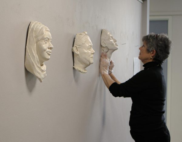Office Administrator for Kidder Hall, Helen Wilhelm, hangs up Vicki Idema’s ‘Miriam Makeba’ clay mask on Feb. 07, 2024