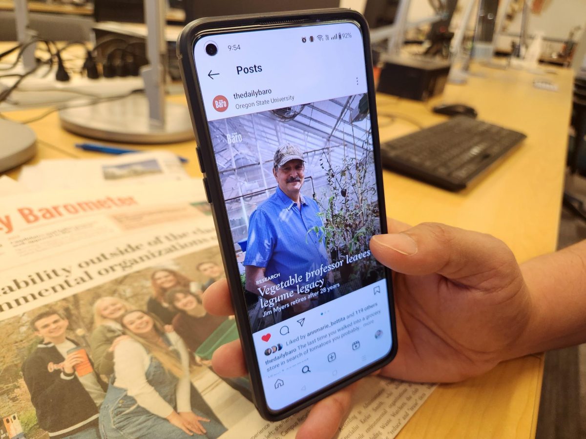 A hand holds a phone pulling up the Daily Barometer Instagram page