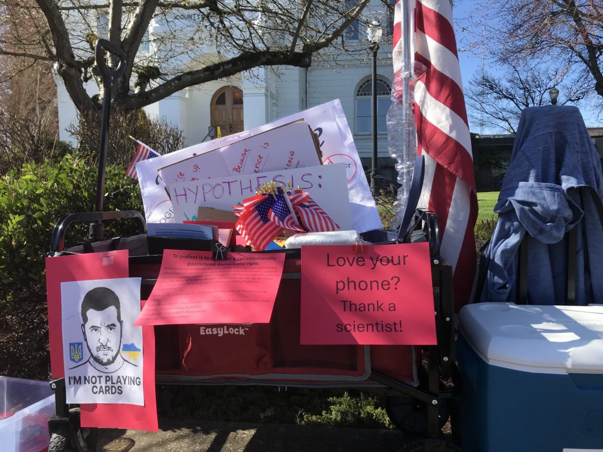 A cart of supplies adorned with signs brought by protester Cheryl Gault sits outside the Benton County Courthouse March 7. Protesters gathered outside the courthouse Friday in opposition to federal cuts to scientific research funding.