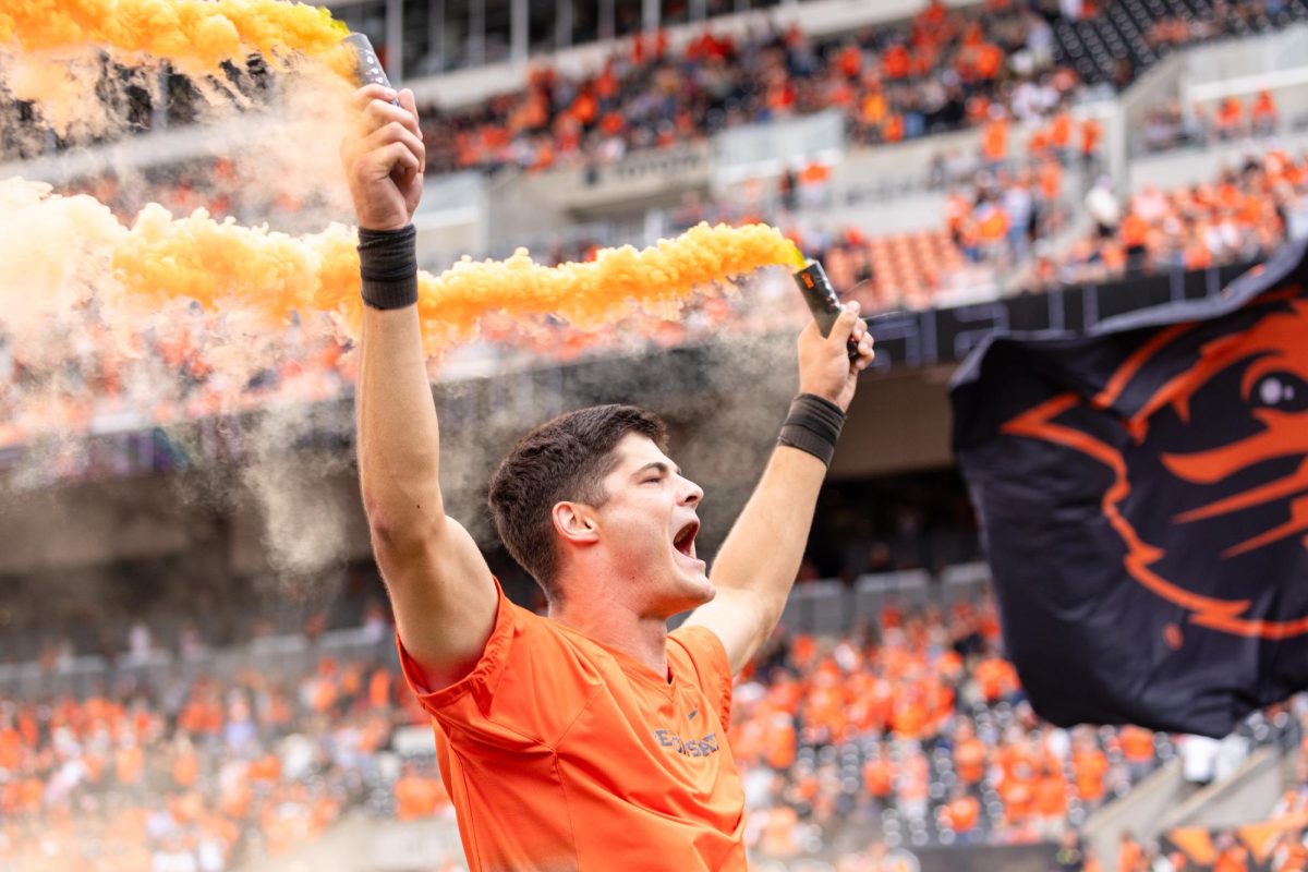 A Oregon State University cheer team member runs towards the student sections with smoke bombs at the game against Fresno State University on Sept. 6, at Reser Stadium.