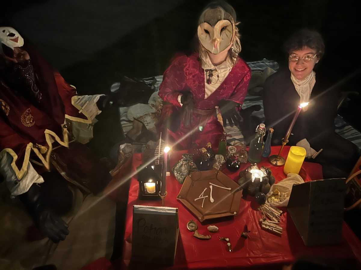 A group of people wearing victorian costumes and masks stand near a table with a red cloth.