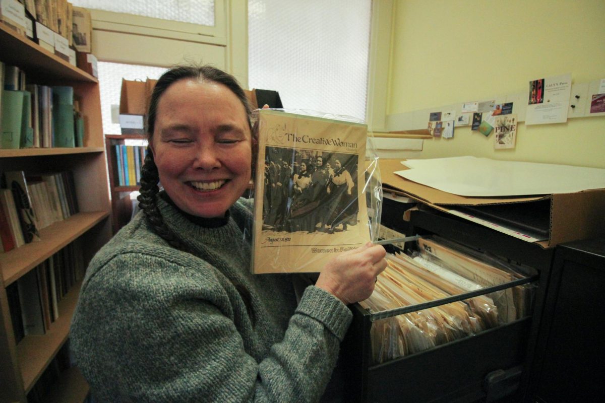 Beth Russell, the Executive Director for Calyx, poses as she holds one of the rarest feminist periodicals of their collection, dating back to the early 1900s, pictured on Feb. 17, 2026 in the Calyx office. The Calyx Press, a by women, for women art and literature journal publishes and stores many pieces of feminist literature from a diverse array of authors.