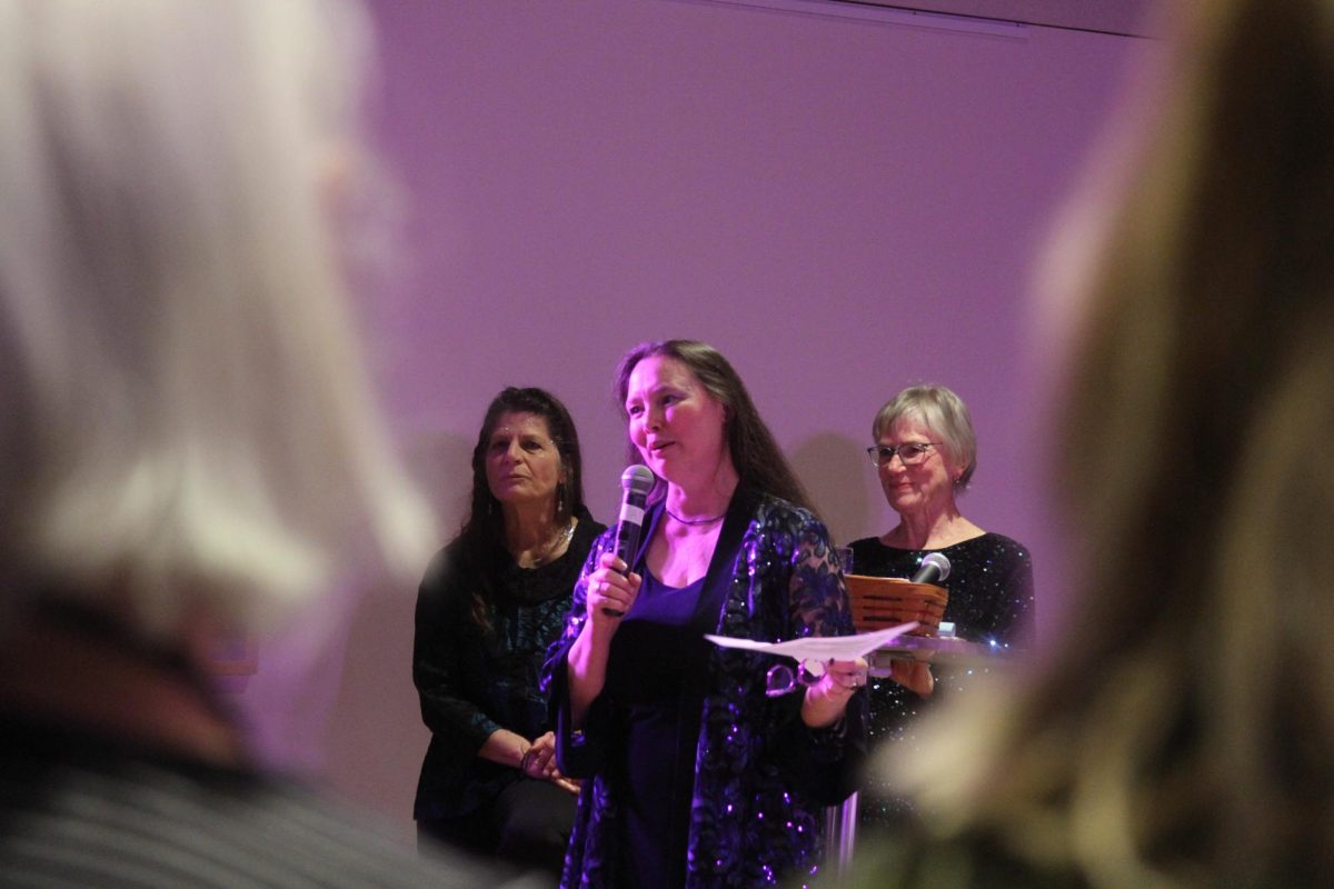 A woman holding a microphone speaks to a group.