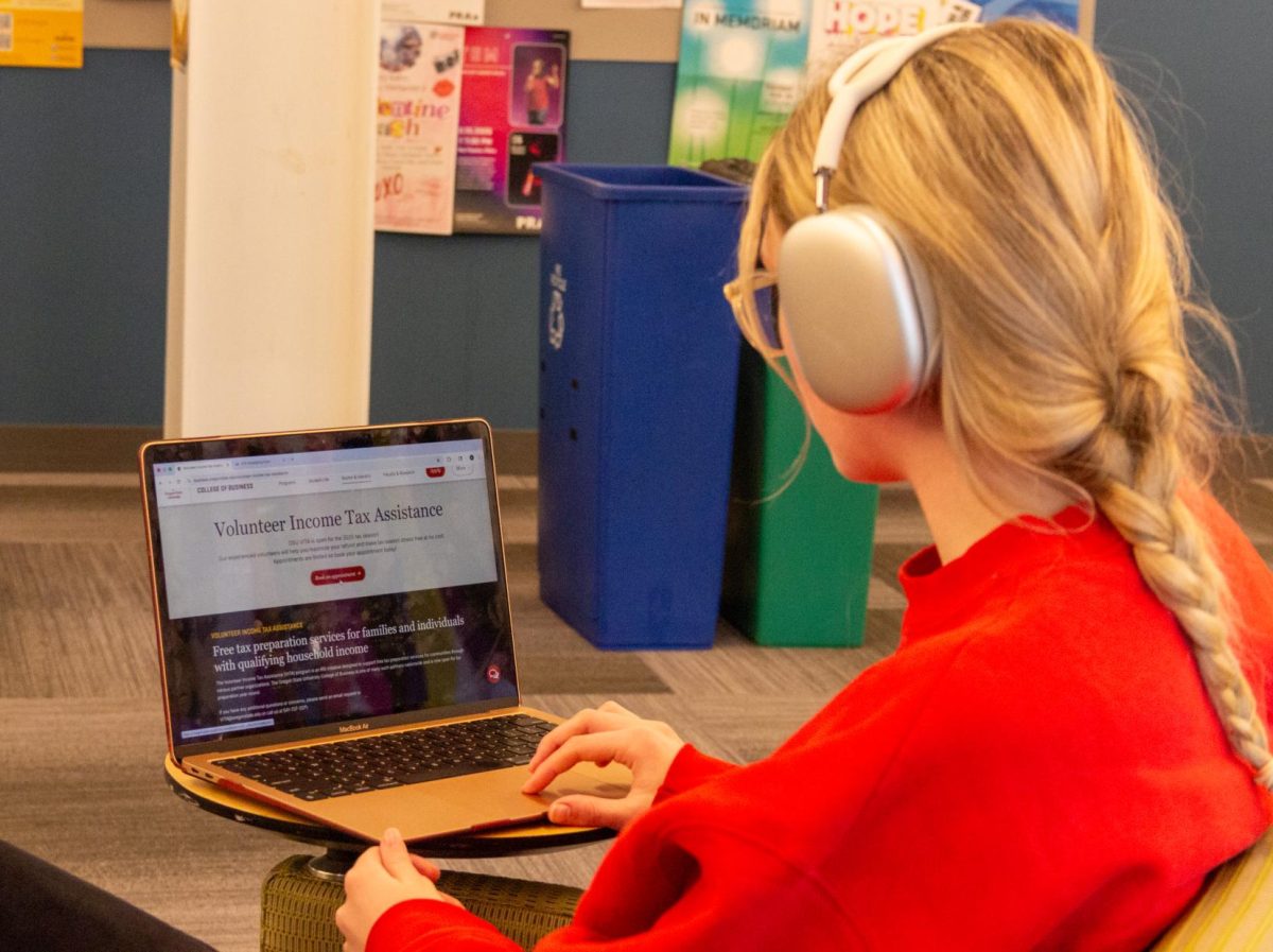 A person wearing headphones sits and looks at a laptop.