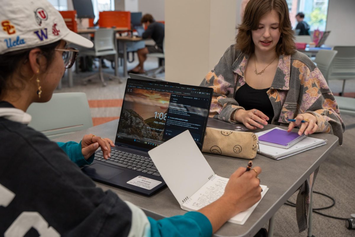 Two women sit with their homework and laptops open.