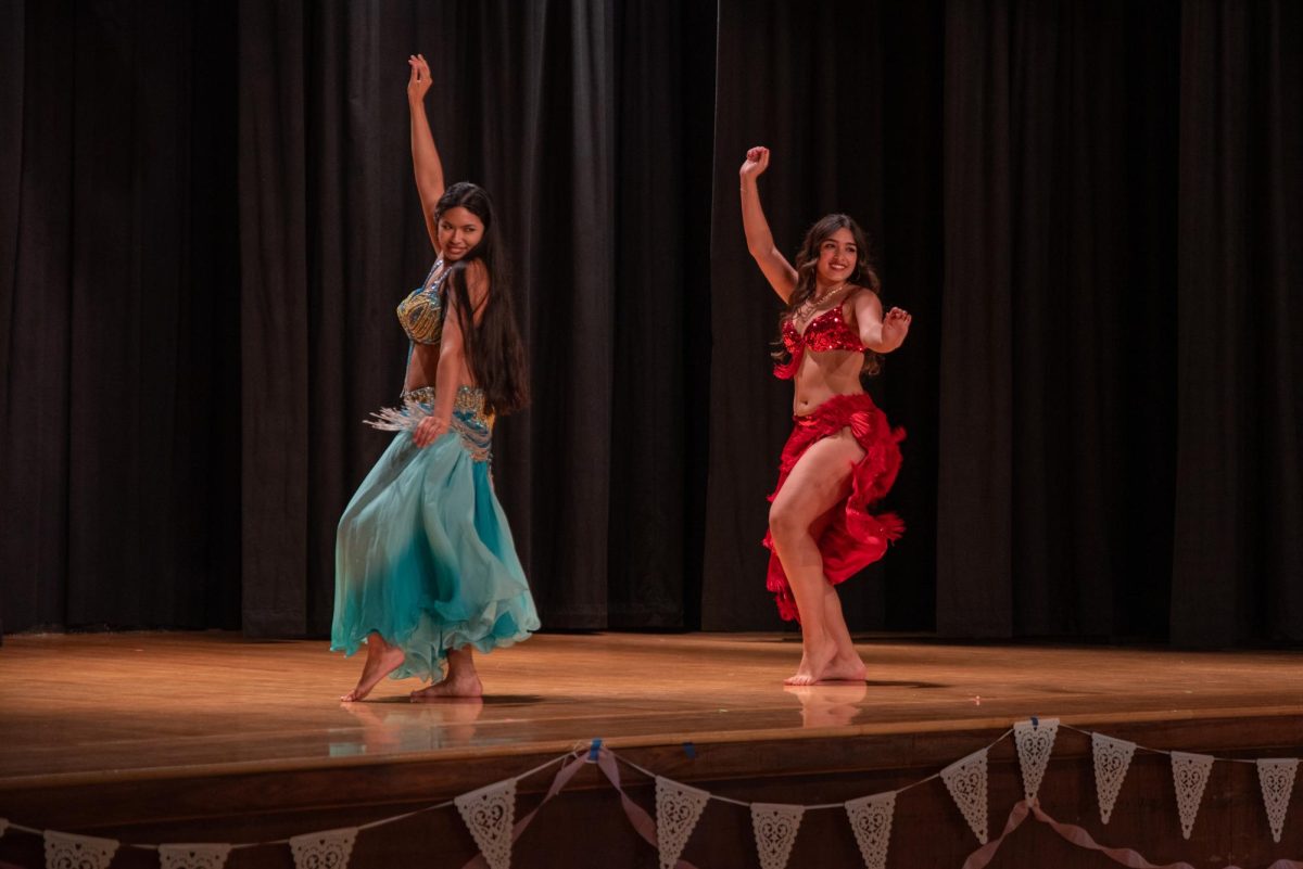Two women dressed in blue and red Middle Eastern dance attire perform a dance on a stage.
