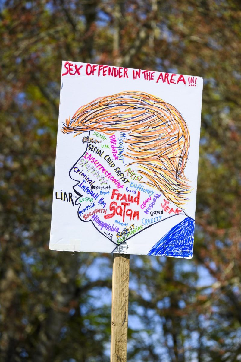 A protest sign is held in the air with tree branches in the background.