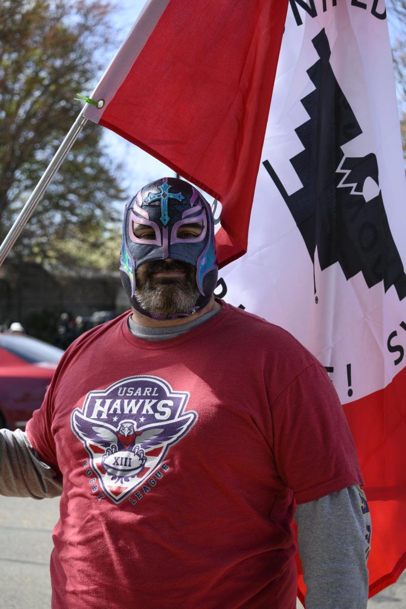 A man poses holding a flag and wears a mask that covers his head.
