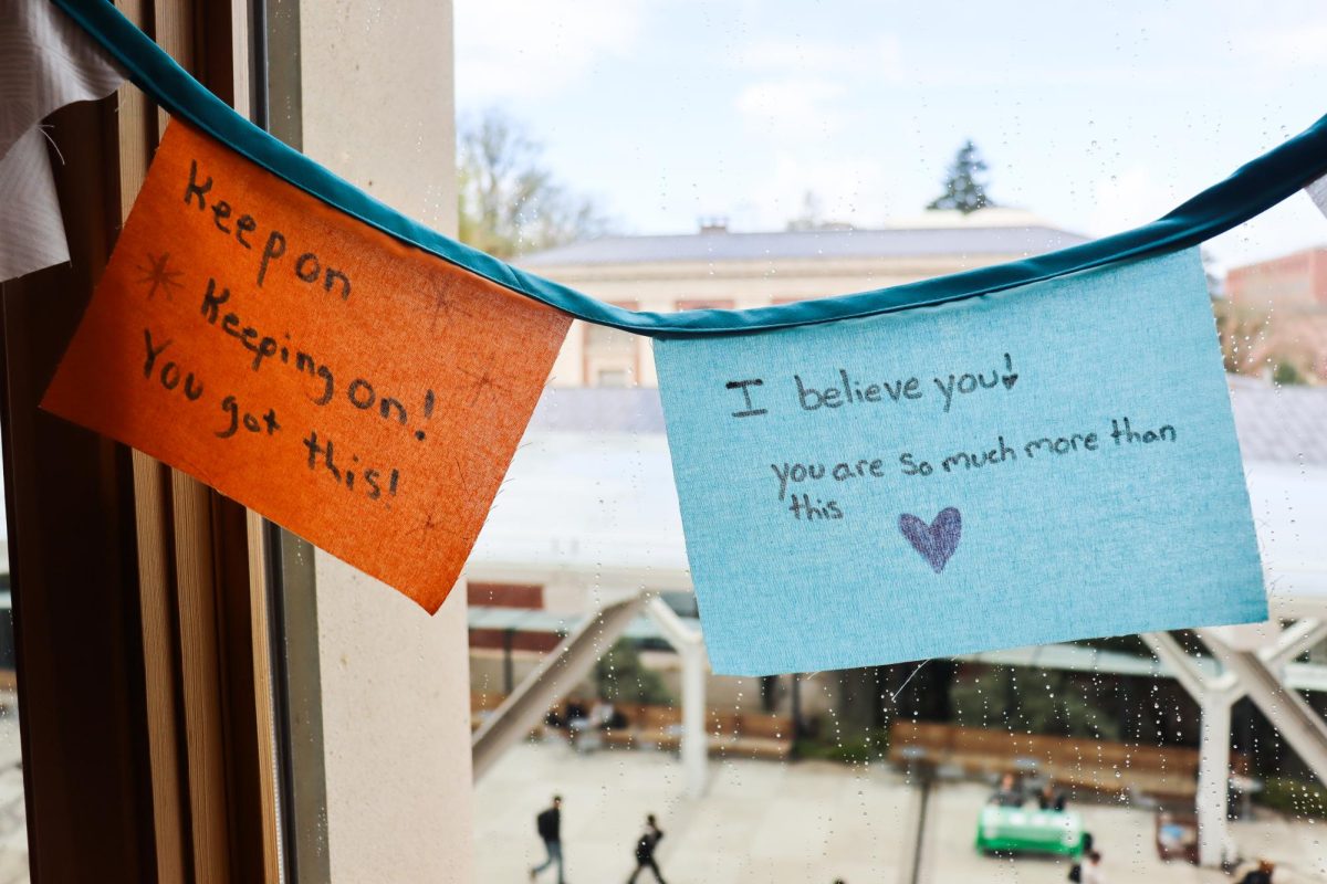 An orange banner hangs to the left of a blue banner in front of a window. The orange banner reads "Keep on keeping on! You got this!" While the blue banner reads, "I believe you! You are so much more than this".