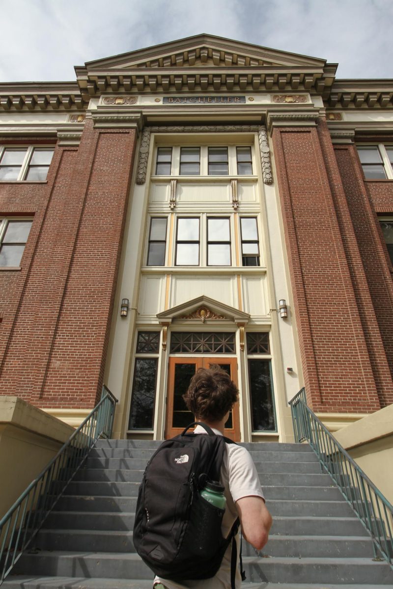 A man with a backpack looks up to the outside entrance of Batcheller Hall.