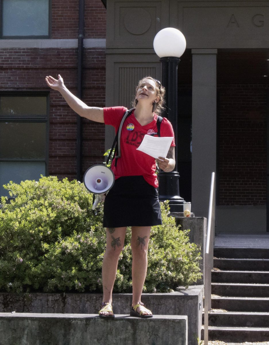 A woman stands on a ledge and makes a gesture while giving a speech.