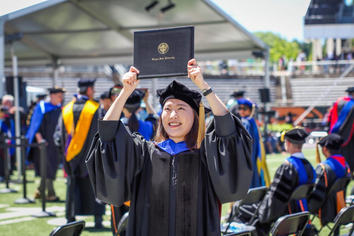 A graduate smiles and holds her diploma above her head.