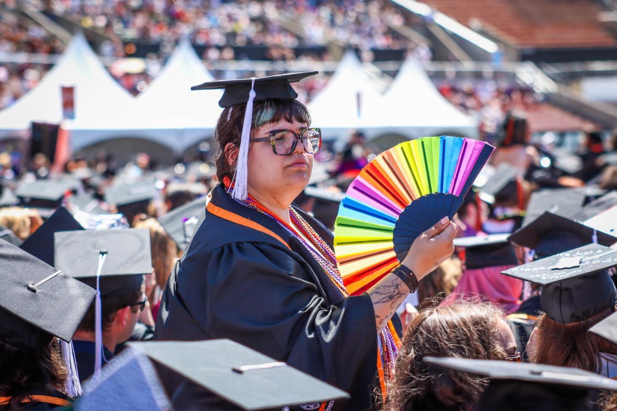 A graduate fans themself with a handheld fan.