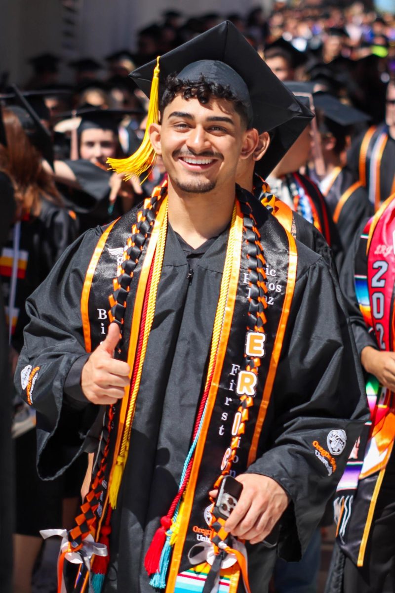 A graduate smiles and walks with a thumbs up.