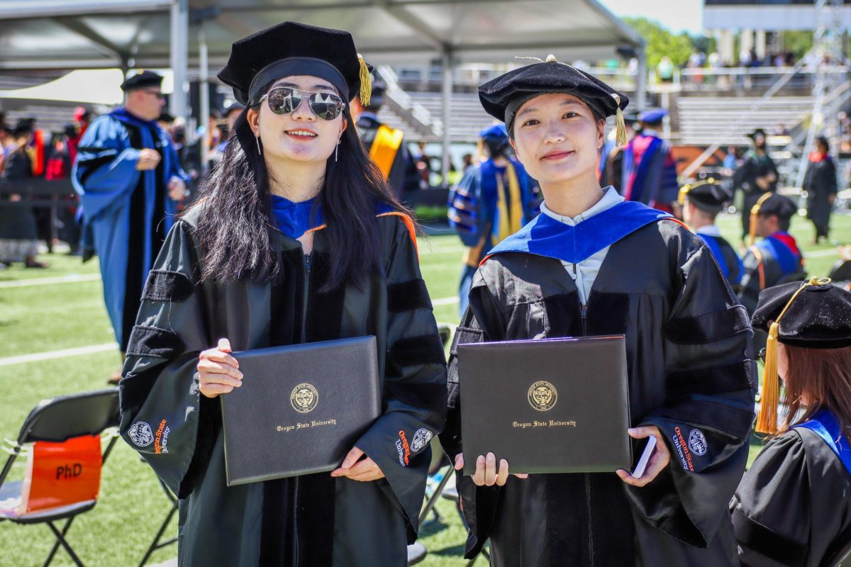 Two graduates pose with their diplomas.