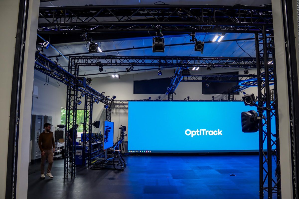 A room surrounded by lightning equipment and other lifted technology. A blue screen glows in the background with text reading OptiiTrack drapes the room in a blue glow.