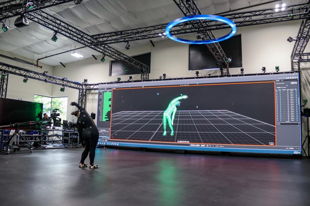 Tiffany Popov, quality assurance manager at OptiTrack, demonstrates the company’s motion tracking technology while wearing a marker-tracking suit inside the facility in Corvallis, on May 14. The space features motion tracking cameras and large display screens used for testing and demonstrations.