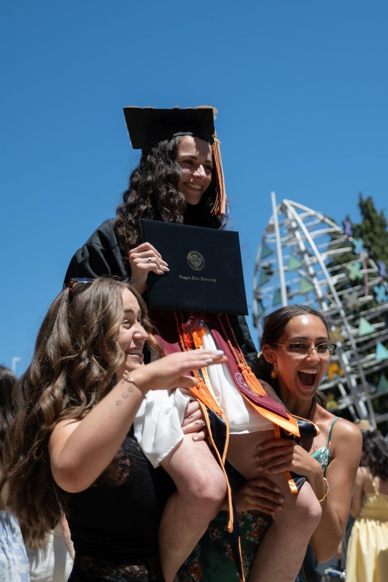 Two people hold a graduate as she sits on their shoulders.