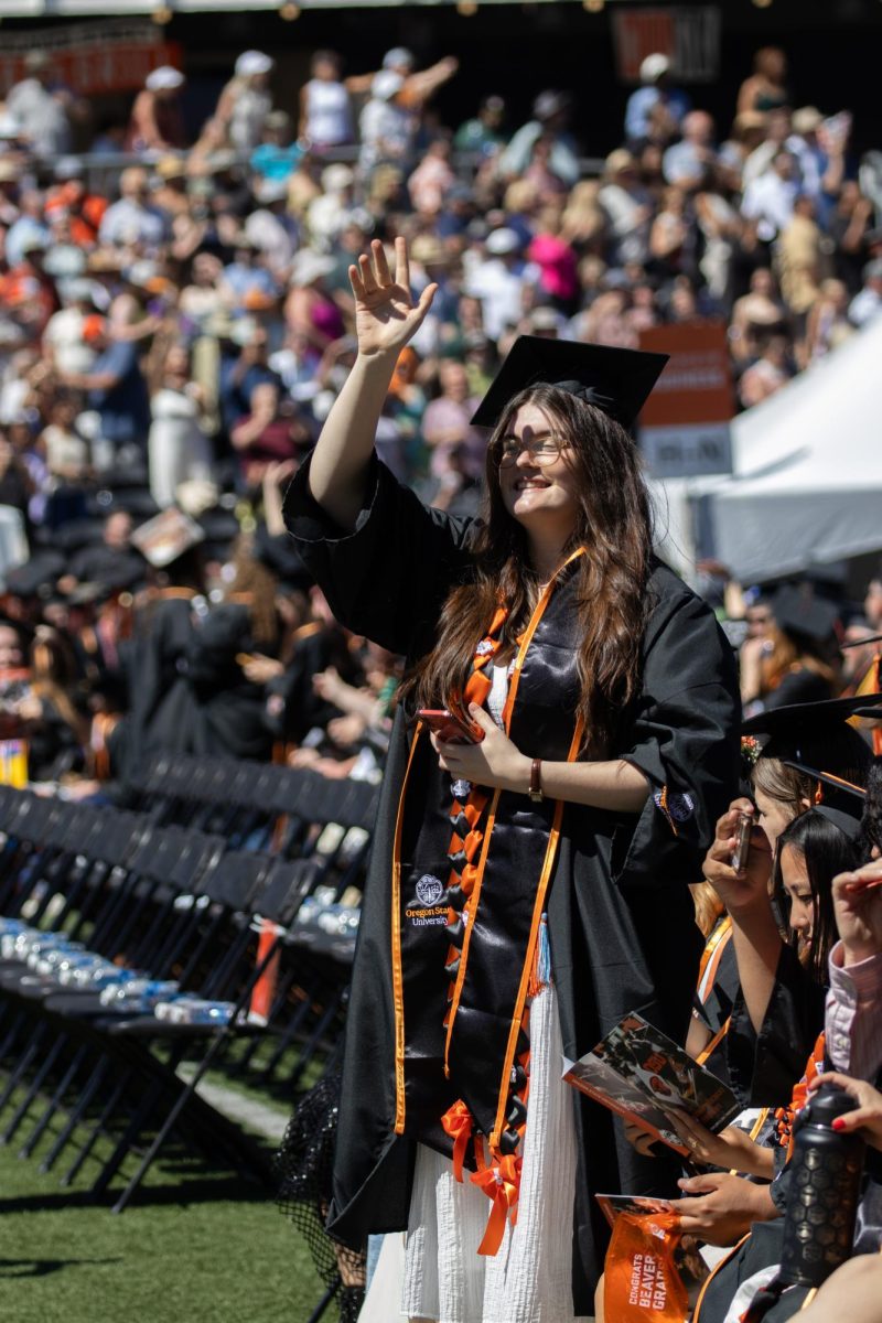 A graduate stands and waves to the crowd from the field.