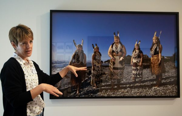 Talking woman stands in front of framed photo.